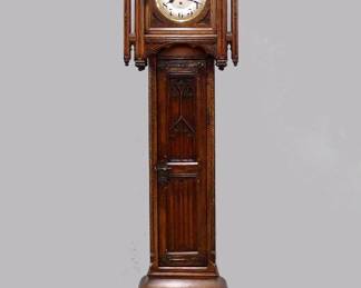 A turn of the century French Gothic Revival tall clock retailed by Dupin & Strembel, Paris.  Junghans 8-day, spring driven time and strike movement with quarter hour strike, Silvered dial and Arabic numerals.  Carved Gothic Revival case with central spire flanked by smaller spires, single door with carved tracery and arched dial glass, central waist door with one arched panel over linen fold panel with arched quarter columns on a stepped base with carved linen fold design and heavy molded foot.  Old finish with very minor wear, running when cataloged, strike needs adjustment.  21 1/2 x 11 1/2 x 102" high overall.