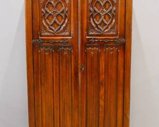 A turn of the century Gothic Revival Period carved Oak armoire.  Molded top over two long doors with carved tracery and linen fold panels, with Iron hinges and lock.  Older dark finish with minor wear.  38 x 18 1/2 x 70 3/4" high overall.