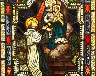 A Gothic Revival stained glass window of Mary's Promise to St. Simon.  Multi-color stained and leaded glass panels with reverse painted detail depicting St. Simon recieving the Scapular from the Madonna and Child within geometric and foliate borders.  Two panels cracked, one with edge chips, touch ups to enameled border, some wear to paint.  In a later Oak frame, 24 x 37 3/4" high overall.
