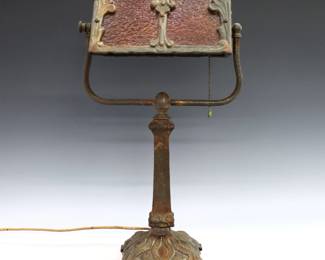 A turn of the century American Arts & Crafts Period Cast Iron desk lamp.  Adjustable foliate shade with Amber glass panels on a cast base with "hammered" texture and patinated finish.  Original finish with wear and some oxidation.  18" high.