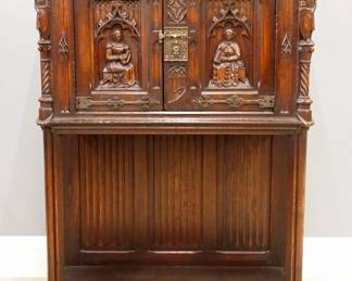 A turn of the century Gothic Revival Period carved Oak court cupboard.  Molded top with canted corners over two doors with carved tracery and figural panels, rope twist columns surmounted by carved Knights, over an open lower shelf with linen fold carved back panel, Iron hinges and figural Apostle lock.  Original "Karcher & Rehn Co., Philadelphia" embossed foil label at back.  Older finish with some wear, rippling to veneer at bottom shelf.  37 1/2 x 19 1/4 x 53 1/2" high overall.