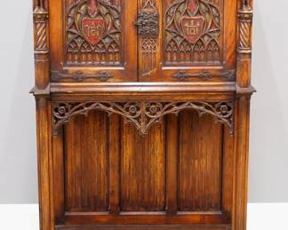 A turn of the century Gothic Revival Period carved Oak court cupboard.  Molded top over two doors with carved tracery, rope twist columns surmounted by carved Knights, over a open lower shelf with linen fold carved back panel, original polychrome detail, Iron hinges and lock.  Original finish with some wear and shrinkage.  38 x 18 x 57" high overall.