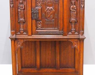 A turn of the century Gothic Revival Period carved Oak court cupboard.  Molded top over one central door with carved tracery and armor, flanked by carved figural panels and spires, over an open lower shelf with linen fold carved back panel, Iron hinges and figural Apostle lock.  Older finish with some wear and minor shrinkage.  38 x 18 1/2 x 54 1/2" high overall.