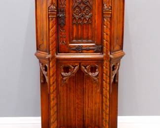 A turn of the century Gothic Revival Period carved Oak side cupboard.  Molded top with canted corners over one central door with carved tracery, rope twist columns surmounted by carved Apostles, over an open lower shelf with linen fold carved back panel, Iron hinges and lock.  Original finish with some wear, marks to top, shrinkage.  27 1/4 x 16 x 53 1/2" high overall.