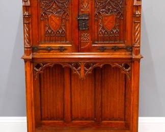 A turn of the century Gothic Revival Period carved Oak court cupboard.  Molded top over two doors with carved tracery, rope twist columns surmounted by carved Knights, over a open lower shelf with linen fold carved back panel, Iron hinges and figural Apostle lock.  Older finish with minor wear.  37 1/2 x 17 3/4 x 57 1/2" high overall.