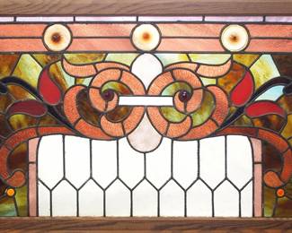 A turn of the century American stained glass window.  Multi-color stained and leaded glass panels depicting a scrolling Lily design with slag, opalescent and faceted glass accents within geometric borders with bullseye and textured glass details.  A few cracked panels, some surface scratches to glass.  In an Oak frame, 42 1/2 x 25" high overall.