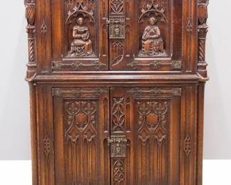 A turn of the century Gothic Revival Period carved Oak linen cupboard.  Molded top with canted corners over two doors with carved figural panels and rope twist columns surmounted by carved Knights, over two lower doors with carved tracery, Iron hinges and figural Apostle locks.  Older finish with minor wear.  38 x 19 1/2 x 53 1/2" high overall.