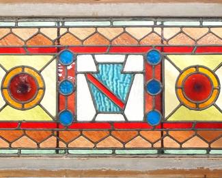 A late 19th century American stained glass transom window.  Multi-color stained and leaded glass panels depicting a geometric design with opalescent and bullseye glass accents.  Several cracked panels, some bowing, braced at back.  In a Pine frame with wear, 37 1/4 x 18 1/4" high overall.