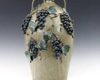 Michael Crocker, American (Georgia), b. 1956.  A contemporary Stoneware Folk Art jug.  Two strap handles and applied Grape Vine decoration with polychrome glaze on a mottled Green ground.  Signed "Michael Crocker" and dated "2005" with "Hand Made in Lulu, Georgia U.S.A." at underside, incised "5" gallon at back of shoulder.  Minor surface wear.  19" high.