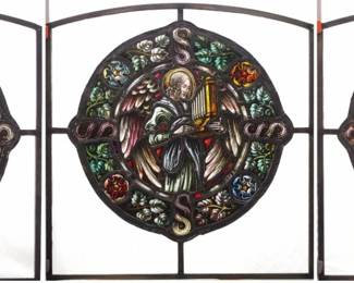 A Gothic Revival French Stained Glass panels of an Angelic Choir.  Medallion form multi-color stained and leaded glass panels with a reverse painted detail depicting three Angels playing musical instruments within foliate and geometric borders with clear glass frame.  Violin and horn windows each have two cracked panels, original medallions with painted restorations, clear glass frames a later addition, some wear to paint.  Each 22 1/2 x 23" high overall.
