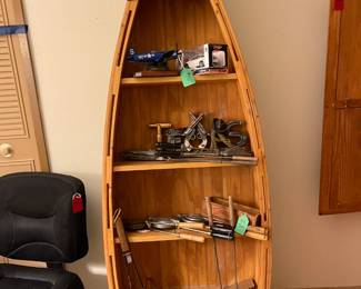 Canoe bookshelf that's filled with vintage campfire cookers, including a 'dog and bun' cooker. 