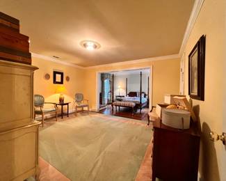 Bedroom 1 | An 11'x12' vintage sage green and salmon area rug, a 1950s Mid-Century Provincial style dresser, a late 20th-century Queen Anne four-poster bed, and several other elegant pieces of vintage or antique furniture.