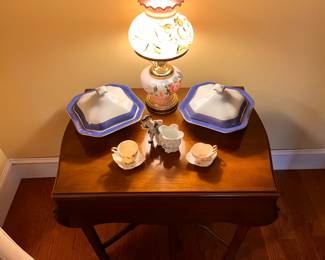 Living Room | On this drop leaf card table is a stunning pair of blue and white octagonal covered serving dishes with gold rims, an antique hand-painted electrified Victorian oil lamp, mismatched cups and saucers, and a figural flower vase.
