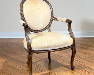 LOUIS XVI STYLE SLIPPER ARM CHAIR | Champagne upholstered Louis XVI slipper chair with fluted arms and floral carved accents over cabriole legs. - l. 27 x w. 24 x h. 36 in

