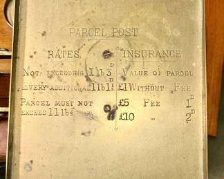 Writing on top of antique brass postal scale with weights on wooden stand
