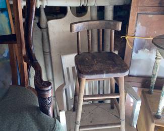 Bed frames behind painted office chair below a primitive child’s high chair 