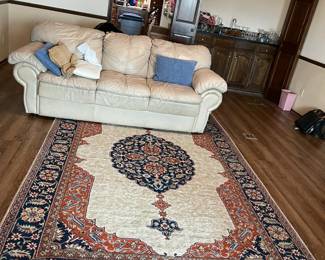 Cream leather sofa and navy, red and cream area rug with fringe.