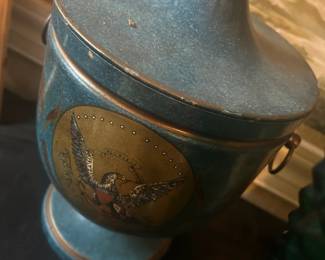 A vintage Italian Tole ice bucket dating from the Mid-century. Inspired by an antique design and manufactured in Italy, this footed urn ice bucket showcases the timeless allure of toleware craftsmanship. Decorated on the front and back with elegant black classical designs against a honey-colored backdrop, it is effortlessly sophisticated. It features a brass finial on the lid and a pair of ring handles on the sides. The inside of the lid and vessel are lined with opaque white plastic, ensuring the protection of the metal and enhancing its functionality. With its fully lined and waterproof design, this tole urn ice bucket combines practicality with aesthetics, making it a stylish addition to your home bar.