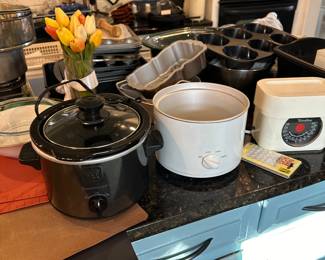 Several crockpots, food scales, baking pans, trays, and molds. Glass pie dishes. cookware
