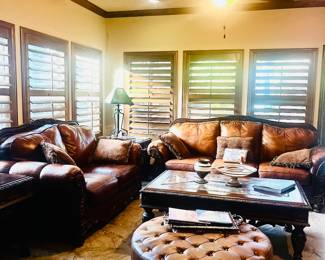 Plush leather and wood matching sofa and love seat, large elegantly tooled coffee table with marble inserts, and tufted leather ottoman.