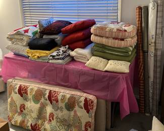 This table has a few pillows on it.  To the right are partial fabric bolts.