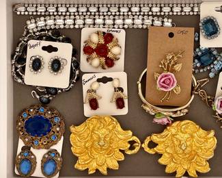 Detail of gorgeous vintage costume jewelry sets including Bogoff post earrings and matching necklace featuring black oval cabochon haloed with rhinestones and set into silver, an Emmons pin and matching pair of Emmons earrings featuring red flowers gold leaf filigrees and milky cream oval cabochons, a Coro pin with matching bracelet featuring a pink rose set into gold leaves, and an ornate blue faceted gemstone and brass filigree pin with matching post earrings.