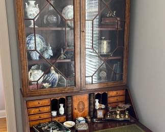 A fine 19th C two part mahogany secretary desk, the upper case with a molded cornice surmounting two glass doors with fretwork, opening to three interior shelves over a lower slant front desk with compartmentalized interior and over four graduated long drawers, all supported by carved bracket feet. The entire piece features cross-banded border veneers on the doors, cover, and drawers, and the top is held in place with pegs.