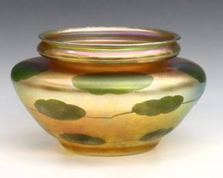 An early 20th century Tiffany Favrile Glass bowl.  Tapered form with molded rim and trailing Lily Pad decoration on an Iridescent Gold ground.  Signed "L.C. Tiffany - Favrile" and "1466 J" at underside.  Slight surface wear.  8" diameter x 5" high overall.  
