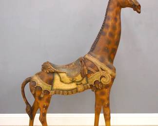 An early 20th century Giraffe Carousel figure by the Philadelphia Toboggan Co., c. 1905.  Hollow body construction with carved detail and original Polychrome painted finish, features the standing figure with inset glass eyes, carved mane and saddle with mask cantle and scrolled trappings with tassel drops.  Some surface wear, chips and minor touch-ups, older restoration to right ear and eye socket, some shrinkage and joint separation, right rear leg loose, some loss to hooves.  78 1/2" high overall.  

