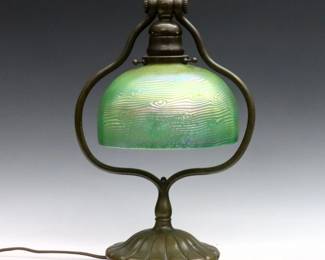 An early 20th Tiffany desk lamp with King Tut shade.  Domed glass shade with swirled Green King Tut pattern decoration, on an adjustable patinated Bronze Harp base with circular foot.  Shade signed "LCT Favrile" at fitter, base double impressed "Tiffany Studios / New York" and "419".  Repaired flakes at fitter, minor wear to patina on base.  Shade is 4 1/4" high with 2" fitter, 13 1/2" high overall. 
