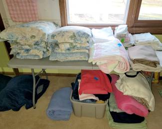 Weighted blanket on floor on left. Twin bedding sets on table on left and other linens and throws (not fill-a-bag)