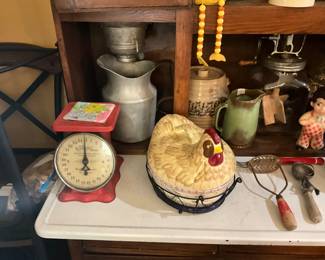Items on Hoosier cabinet - scale, metal pitcher,  canister with lid, vintage glass churn with wooden paddles, Stoney Big Boy, vintage utensils, ceramic  2 piece  chicken in wire basket.  