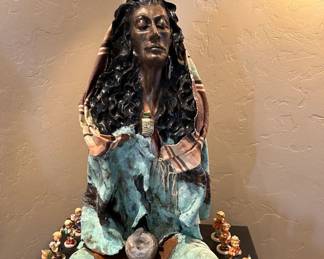 Resin and mixed media art sculpture of a seated woman.  Also known to us as Mama Hummel surrounded by her children.