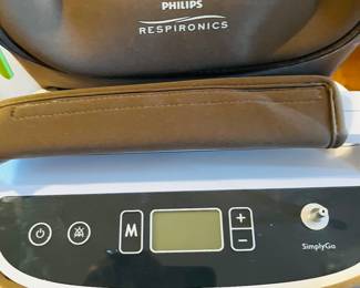 Simply Go oxygen concentrator with accessories, oxygen concentrator, 2 unused canulas, 2 rechargeable batteries plus external battery charger, travel cart, AC power supply, DC power supply, Phillips Respironics carrying case with shoulder strap for concentrator, Phillips Respironics accessory bag for extra battery, bag for cords, and bubble humidifier