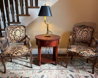 Living Room:  Two separately priced antique French Louis XV-style armchairs have raised velvet upholstery on the front but black "leather" upholstery on the back.   They flank an oval table with one drawer and an under-shelf as well as a vintage brass horn lamp with black paper shade.  Closer photos of the chairs follow.