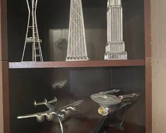 Bookshelves displaying a set of wire building sculptures, a Star Trek Enterprise display figure, and an Art Deco metal airplane on a globe stand