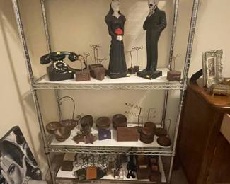 A display rack full of jewelry displays/hangers and wooden bowls, plus a black Bakelite rotary telephone and a large skeleton couple figurine set