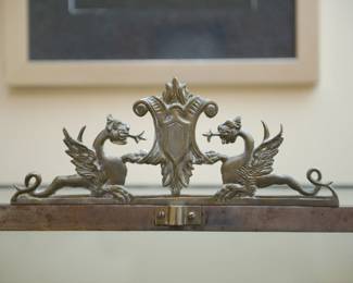 Sculptural dragons framing a crest top detail of cast iron and glass vitrine or display case with decorative finials and two sculptural dragons at the top center with two glass doors