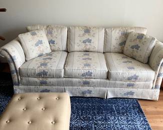 Cream floral three cushion sofa, faux leather ottoman, blue rug