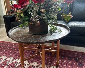 Moroccan 6 leg Wooden Folding Table with Brass Tray. Pakistani Bokhara rug, Natuzzi black leather sofa, floral arrangement in hammered copper pot
