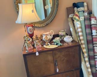 MIRRO, LAMP, BOLTS OF MATERIAL, AND ODDS AND ENDS, ON TOP OF A SMALL STORAGE CHEST 