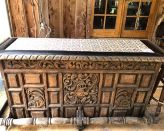 Vintage all hand carved Mediterranean Tiki Bar. It has tile on the bar top.  Faux black leather padded elbow rest with metal tacks.  Foot rail.  Back of bar has two side cabinets and five drawers for storage.  
