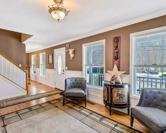 Welcome to a space where classic charm meets modern relaxation. This elegant hallway extends a warm invitation to guests, featuring a comfortable sitting area with two chic, patterned armchairs, ideal for intimate conversations or a quiet reading nook. The area is adorned with tasteful art pieces and a functional yet stylish console table, providing the perfect spot to showcase decorative accents. Natural light floods the space through large windows, creating an inviting ambiance. This well-appointed area bridges functionality and aesthetic appeal, offering a preview of the home's welcoming spirit.