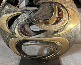 The intricate metallic sculpture in the image appears to be an abstract piece, featuring intertwined elements with textured surfaces.
