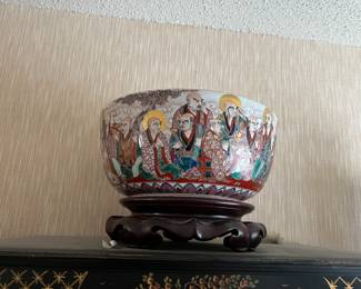 This 12-inch diameter 20th century Japanese Kutani hand-painted gilt bowl on carved wooden stand depicts the immortals, who represent good luck, fortune, peace and happiness. Each immortal has his own wonderfully characterful face, with a few having dramatically drooping ears and eyebrows! $600