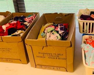 Boxes filled with baby girl gowns, play clothes and shorts and shirts. 