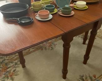 Early handmade mahogany drop leaf table with turned legs and a partial set of Russell Wright American Modern dinnerware 