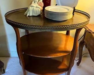 A vintage mahogany three tiered parlor table.  Features a brass gallery with leather top and two lower mahogany shelves. 