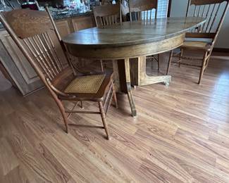 Split Leaf pedestal round oak table with leaves. Set of 4 pressed back oak chairs. NOTE: how the pedestal is opened to show that it is a split pedestal to help better support the table ends as more leaves are added. 