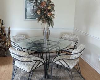 Beautiful modern glass top table and 4 chairs, metal sculpture piece in the background 